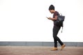 Full body side of african american man walking with bag and listening to music with smart phone