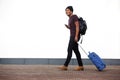 Full body side of african american man walking with suitcase and mobile phone by white wall Royalty Free Stock Photo