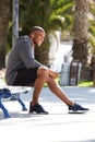 Full body portrait of fit black guy sitting on bench and listening music Royalty Free Stock Photo