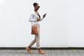 Side portrait young african american woman walking against white wall with cellphone Royalty Free Stock Photo