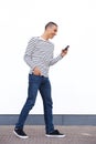Side portrait of young man walking and looking at cellphone by white wall Royalty Free Stock Photo