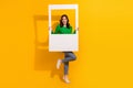Full body size photo of friendly lady wear green jumper and jeans hold paper frame photozone window on yellow