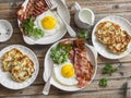 Full breakfast table - fried eggs with bacon and potatoes, green peas, leek pancakes on a wooden table