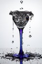 Full cocktail glass on blue thin and high leg with frozen water streams and flying water drops on dark glossy surface in white Royalty Free Stock Photo