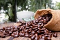 Full of coffee beans spilling out bag on brown wooden background with a cup of black coffee Royalty Free Stock Photo