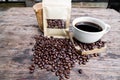 Full of coffee beans spilling out bag on brown wooden background with a cup of black coffee Royalty Free Stock Photo