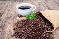 Full of coffee beans spilling out bag on brown wooden background with a cup of black coffee Royalty Free Stock Photo