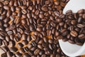 Full of coffee beans spilling out white ceramic cup on brown wooden background Royalty Free Stock Photo