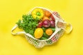 Full eco mesh bag of different health food - bell pepper, tomatoes, cilantro, leemon, green, cucumber, onions on yellow background Royalty Free Stock Photo