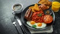 Full English breakfast with bacon, sausage, fried egg, baked beans, hash browns and mushrooms in black plate. cup coffe Royalty Free Stock Photo