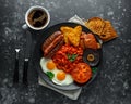 Full English breakfast with bacon, sausage, fried egg, baked beans, hash browns and mushrooms in black plate. cup coffee. Royalty Free Stock Photo