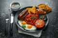 Full English breakfast with bacon, sausage, fried egg, baked beans, hash browns and mushrooms in black plate. cup coffee. Royalty Free Stock Photo