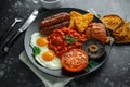 Full English breakfast with bacon, sausage, fried egg, baked beans, hash browns and mushrooms in black plate. cup coffee. Royalty Free Stock Photo