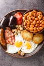 Full English breakfast with bacon, sausage, fried egg, baked beans, hash browns and mushrooms closeup in the plate. Vertical top Royalty Free Stock Photo