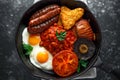 Full English breakfast with bacon, sausage, fried egg, baked beans, hash browns and mushrooms in rustic skillet, pan.