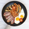 Full English Breakfast in a cooking pan with sausages, fried eggs, beans and bacon on a white wooden table, top view. Flat lay. Royalty Free Stock Photo