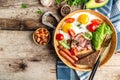 Full English Breakfast with fried eggs, bacon, beans, toasts, tomatoes, sausages and avocado on wooden background. Top view, Royalty Free Stock Photo