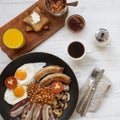 Full English breakfast in a pan with fried eggs, bacon, beans, sausages  and toasts on white wooden surface, top view. Flat lay. Royalty Free Stock Photo