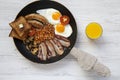 Full English breakfast in a pan with fried eggs, bacon, sausages, beans, toasts and orange juice on white wooden background, top v Royalty Free Stock Photo