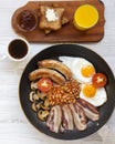 Full English breakfast in a pan with fried eggs, bacon, sausages, beans and toasts on white wooden surface, top view. Flat lay. Royalty Free Stock Photo