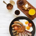 Full English breakfast in a pan with fried eggs, bacon, sausages, beans and toasts on white wooden table, overhead view. Flat lay Royalty Free Stock Photo