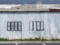 full frame close up of a shabby old dilapidated corrugated iron building with with closed painted over patched windows repaired Royalty Free Stock Photo