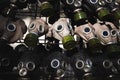 A full frame dark image of rows of gas masks with bright green filters on them and blue glass eyepieces