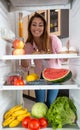 Full fridge concept, young woman enjoying the sight of fruits, vegetables, and all other kinds of foods in her refrigerator