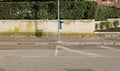 Full garbage bin on a pole in the sidewalk. Concrete fence with hedge on background and asphalt road in front. Royalty Free Stock Photo