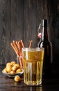 Full glass of beer, bottle and snacks, black wooden background Royalty Free Stock Photo