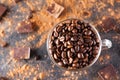 Full glass cup of Roasted coffee beans on the dark stone background with dissipate cocoa, pieces of chocolate and beans. Selective Royalty Free Stock Photo