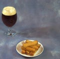 A full glass of dark beer with foam and a plate with wheat croutons on a gray background