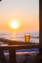 Full glass of light beer against backdrop of dawn on beach