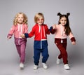 Three active kids two girls and a boy in modern sportswear run together holding hands.