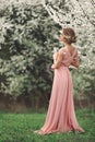 Full height portrait of a young blonde woman in pink dress standing near the blooming cherry tree Royalty Free Stock Photo