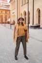 Full height self confident girl in an autumn beige coat and sunglasses, plaid panama hat standing posing on the street