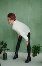 Full height studio portrait of tall young fashion model wearing white sweater and black leather leggings possing at