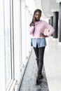 Full height of young afro american woman talking mobile phone in front of panoramic window in comercial center Royalty Free Stock Photo