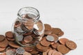 Full jar of coins on a table, surrounded by loose change. Money savings concept with copy space Royalty Free Stock Photo