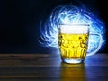 Full jar of lager beer with froth on a wooden table glowing in a dark, blue light painting in the background behind the glass. Royalty Free Stock Photo