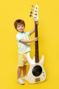 Full lengh photo of funny kid play white electric bass guitar over yellow background.