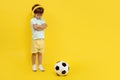 Full lengh photo of sad little boy with soccer ball wearing headphone over yellow background. Royalty Free Stock Photo