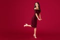 Full lengh portrait of elegant young woman in maroon dress over red background.