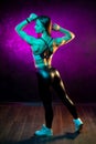 Full lenght photo of beautiful young woman fitness model posing in neon lights in the studio. Sporty woman show her back Royalty Free Stock Photo