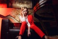 Full-lenght photo of young blonde in red jacket sitting on leather sofa Royalty Free Stock Photo