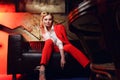 Full-lenght photo of young blonde woman in red jacket looking at camera sitting on leather sofa Royalty Free Stock Photo