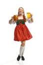 Full-lenght portrait of friendly young woman wearing folk German dirndl with two beer mugs over white background Royalty Free Stock Photo