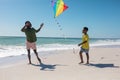 Full length of african american father and son running with kite at beach against clear blue sky Royalty Free Stock Photo