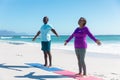 Full length of african american retired senior couple practicing yoga at beach against blue sky Royalty Free Stock Photo