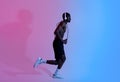 Full length of athletic black guy with bare chest wearing headphones and skipping rope, running in neon light, side view Royalty Free Stock Photo